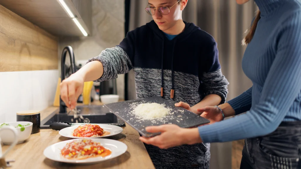 Bespaar geld als kotstudent_ twee studenten die kaas op pasta strooien